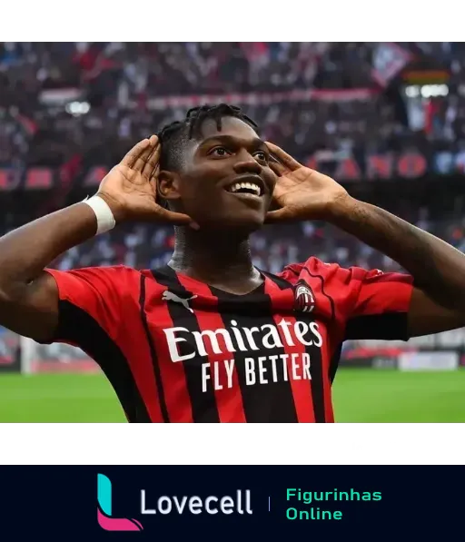 Jogador do Milan celebrando com uniforme preto e vermelho da Emirates Fly Better, sorrindo e fazendo gesto de escuta