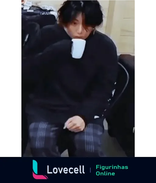 Membro do BTS sentado, vestindo uma blusa preta e calça listrada, segurando uma xícara de café com uma expressão pensativa.