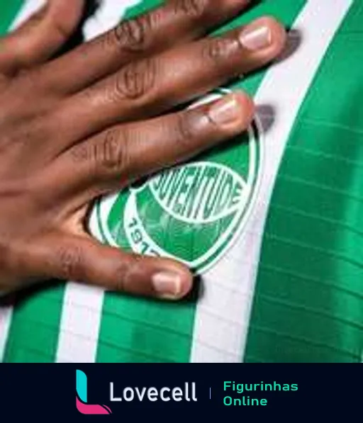 Mão tocando o escudo do Esporte Clube Juventude, com cores verde e branca e o ano de fundação 1913, destacando a tradição no futebol