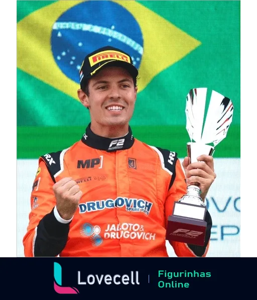 Felipe Drugovich, piloto de corrida, com macacão laranja, sorrindo e segurando um troféu enquanto comemora vitória, com bandeira do Brasil ao fundo