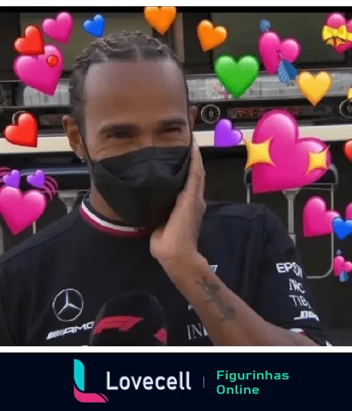 Lewis Hamilton com máscara preta e camiseta escura tocando o rosto com uma mão e corações coloridos flutuando ao redor, expressando amor e carinho