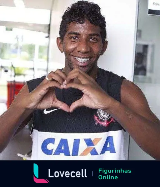 Jogador do Corinthians fazendo gesto de coração com as mãos, sorrindo, vestindo camiseta de treino com logo da Caixa, fundo claro