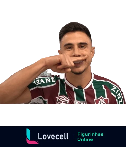 Jogador do Fluminense comemorando com a mão sobre a boca, vestindo uniforme verde, grená e branco com patrocínios