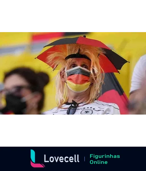 Torcedor da Alemanha em um estádio, usando máscara colorida com as cores da bandeira e um chapéu pequeno com guarda-chuva. Camiseta branca com logotipo da seleção.