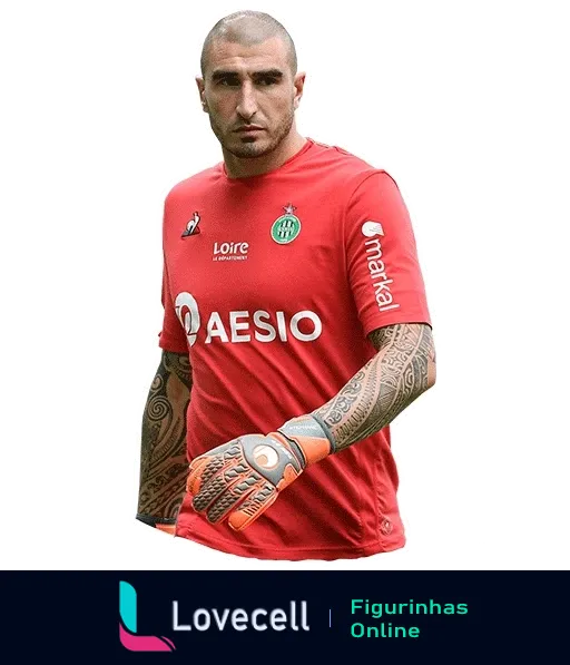 Goleiro do Saint-Étienne em uniforme vermelho, com logos da Aesio e Manlio, mostrando tatuagens nos braços e expressão concentrada