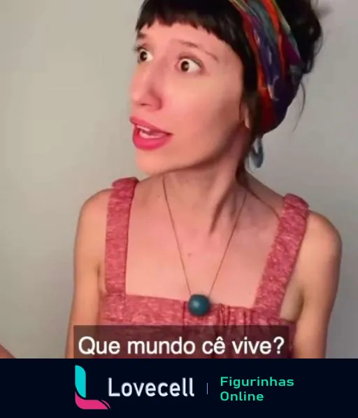 Mulher com lenço colorido e vestido rosa expressando surpresa e questionando 'Que mundo cê vive?' em uma figurinha de WhatsApp