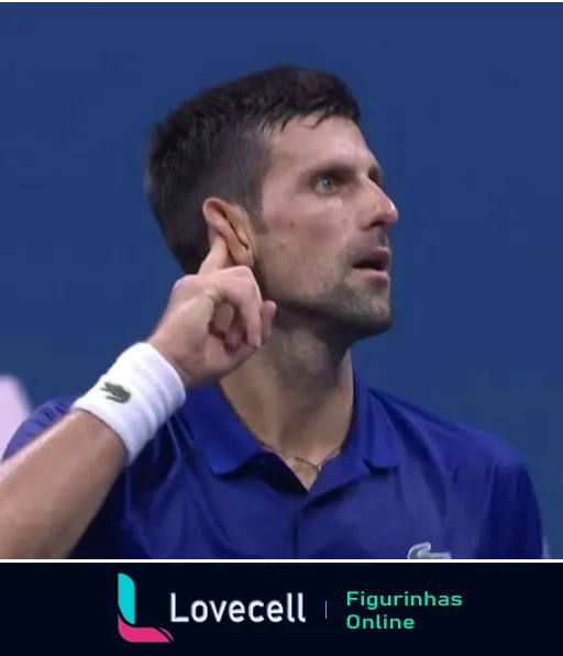 Novak Djokovic em quadra de tênis levantando a mão esquerda ao ouvido, com expressão focada, vestindo camisa polo azul com logos de patrocinadores, ouvindo a torcida