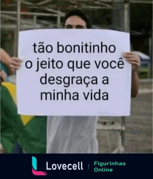 Pessoa segurando cartaz com a frase 'tão bonitinho o jeito que você desgraça a minha vida', expressando indireta de descontentamento.