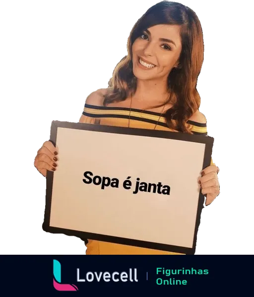 Titi Müller sorridente segurando cartaz 'Sopa é janta' com top listrado amarelo e preto, fundo desfocado