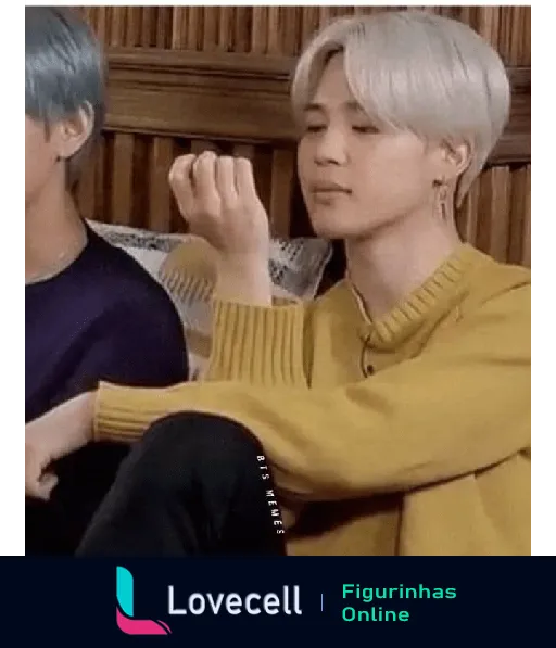 Membro da banda BTS com cabelo loiro platinado e suéter amarelo, observando atentamente suas unhas em uma cena descontraída.