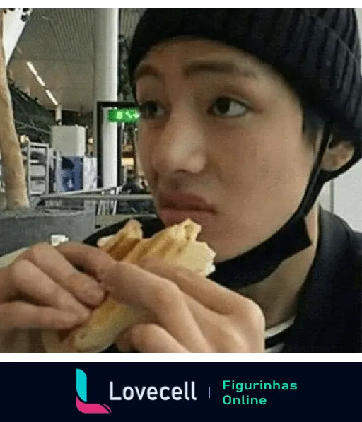 Membro do BTS comendo sanduíche, expressão facial engraçada enquanto segura o lanche com ambas as mãos, usando gorro preto.