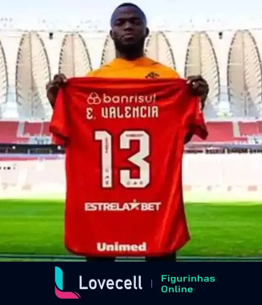 Jogador segurando nova camisa do Internacional número 13 em estádio, camisa vermelha com logos do Banrisul, E. Valencia e EstrelxBet