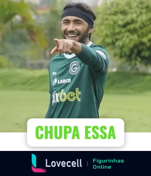 Jogador do Goiás com uniforme verde e faixa na cabeça sorrindo e apontando para frente com a frase 'CHUPA ESSA' destacada, expressando vitória ou desafio