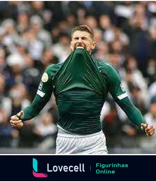 Jogador do Goiás celebrando euforicamente em campo, com uniforme verde, puxando a camisa sobre o rosto