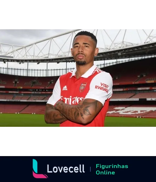 Jogador do Arsenal com uniforme oficial, braços cruzados e expressão séria, com tatuagens visíveis e estádio ao fundo