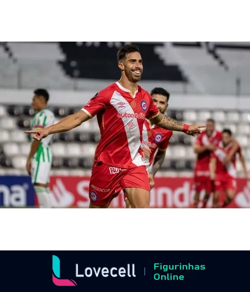 Jogador do Argentinos Juniors celebrando gol com braços abertos e sorriso, vestindo uniforme vermelho e branco