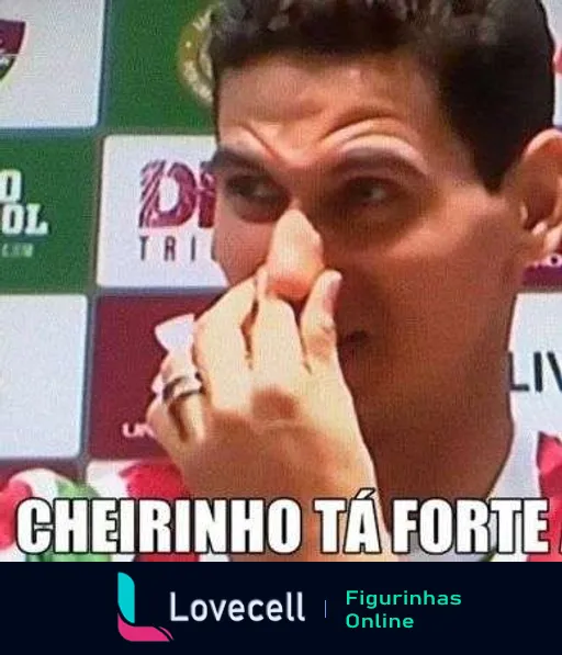 Figurinha de homem parecendo jogador ou técnico de futebol, com dedo no nariz, em sala com logos do Fluminense, frase 'CHEIRINHO TÁ FORTE' em destaque