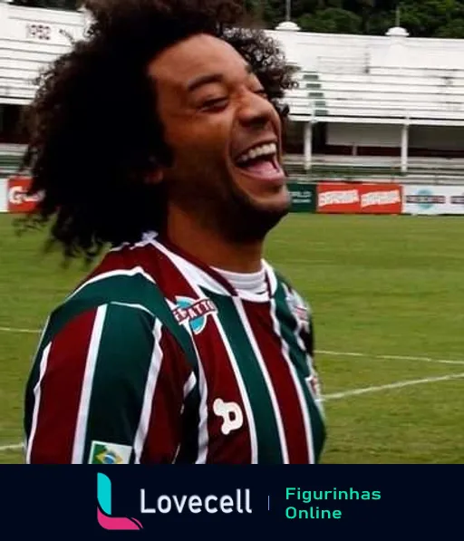 Jogador do Fluminense com cabelos cacheados e negros sorrindo contagiantemente no campo de futebol, vestindo o uniforme com escudo e patrocínios