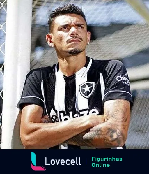 Jogador masculino do Botafogo com camisa do time posando pensativo ao lado de uma rede de gol, exibindo tatuagens nos braços